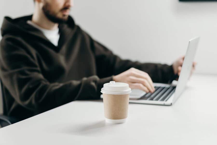 homem com copo de cafeteria digitando em notebook