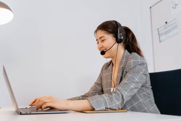 mulher usa headset, e sorri enquanto digita em notebook