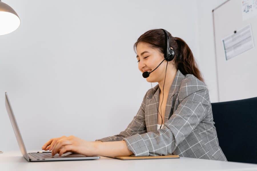 mulher usa headset, e sorri enquanto digita em notebook