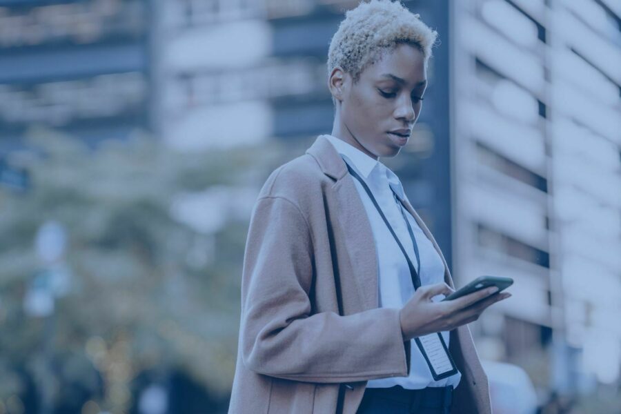 colaboradora na rua com crachá mexe em seu mobile empresarial